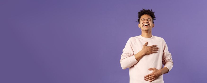 Portrait of cheerful, happy young hipster guy laughing out loud from hilarious joke, watching awesome stand-up performer, chuckle and touchign chest, bending backwards from laugh.