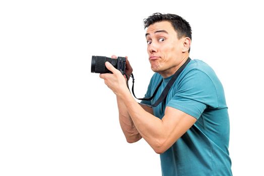 Side view of hilarious male photographer with professional photo camera grimacing and looking at camera against white isolated background