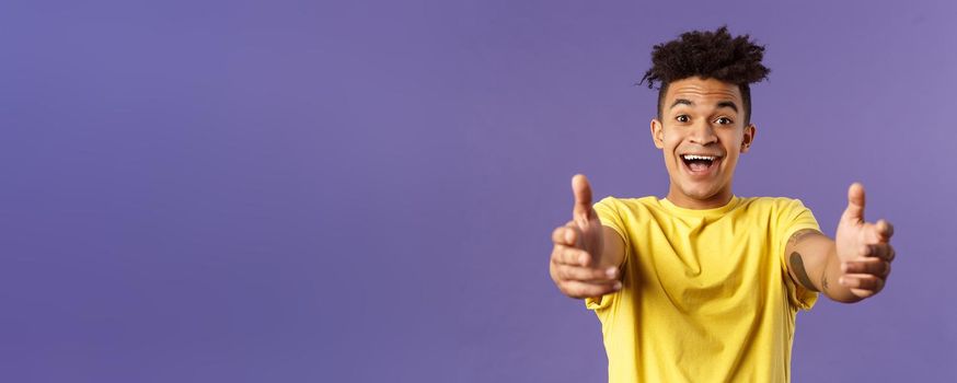 Close-up portrait of charismatic, happy friendly-looking hispanic man with dreads reaching hands forward to hold something, give hug or cuddle dearly, standing purple background.