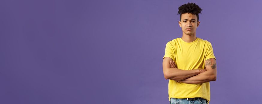 Close-up portrait of skeptical, unimpressed young man with dreads, look judgemental and uninterested, cross arms chest, go on impress me, smirk disappointed, purple background.