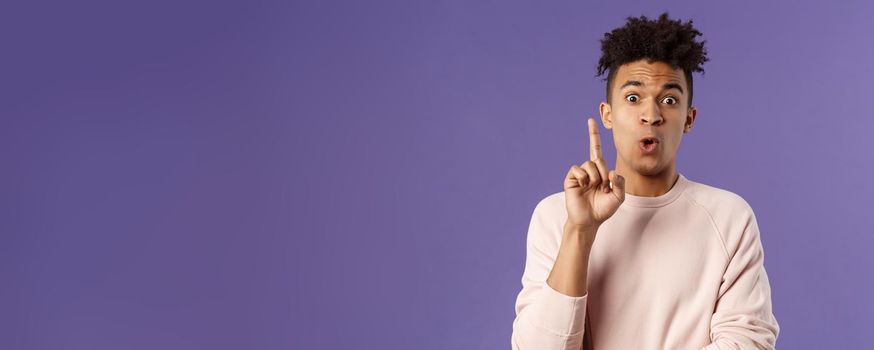 Got it, have plan. Portrait of excited happy young man, rejoicing as being striked with great idea, raise index finger in eureka gesture, figured out something, have suggestion, purple background.