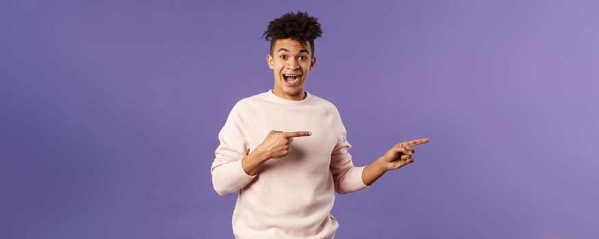 Portrait of enthusiastic lively hipster male 25s, pointing fingers right inviting join courses, sign up for awesome deal, best delivery service or online shop, look amused and happy camera.