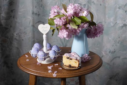 Easter cake and painted eggs and a bouquet of pink sakura flowers on a table in a decorated spring room, a beautiful still life. High quality photo