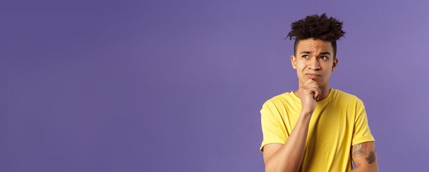 Close-up portrait of indecisive, puzzled attractive young man have problems, lacking idea, thinking, look away frowning and grimacing troubled, standing thoughtful purple background.