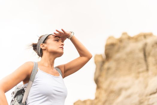 Side view of female explorer shielding eyes from sun and looking away in distance on blurred background of mountain in Tabernas desert