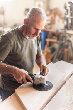 Person operating with a hand sander over a wooden board, vertical picture