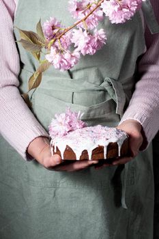 a woman decorates a homemade Easter cake with pink sakura flowers, spring blossom, a bouquet of pink sakura flowers on a table in a decorated spring room, a beautiful still life. High quality photo