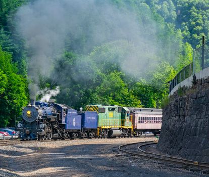 Jim Thorpe, Pennsylvania, July 09, 2022 - A View of a Restored Steam Passenger Train Blowing Smoke and Steam Traveling Pulling Out of a Station on a Sunny Day