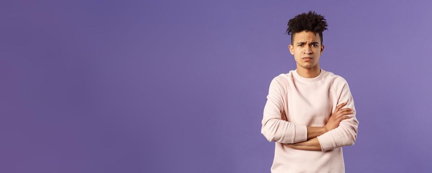 Portrait of young offended hispanic boyfriend, frowning and looking judgemental upset at camera, cross hands over chest defensive insulted pose, standing purple background angry at someone.