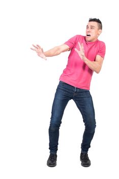 Full length terrified male in jeans and pink t shirt making protective gesture and looking away while yelling in horror against white background