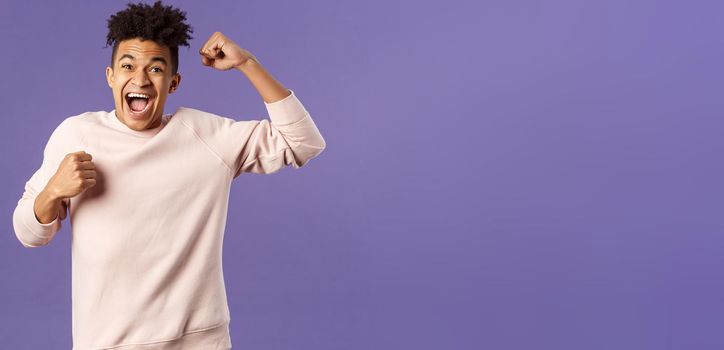 Portrait of excited happy man seeing his team scored goal on sports tv channel, chanting raise one hand in triumph, screaming in joy and happiness, celebrating victory, placed right bet.