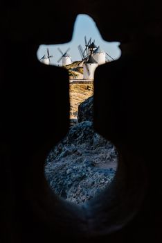 Silhouette of a cross-shaped keyhole with views of windmills in the background of the image in Consuegra, Spain