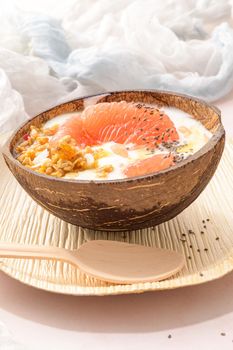 Yogurt with grapefruit, granola, chia and honey served in half a coconut shell on a rose marble kitchen countertop.