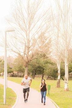 Fitness couple running in the park. Multi-ethnic people exercising outdoors.