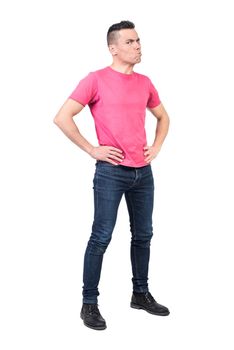 Full body of displeased male model standing with hands on waist and showing anger expression while looking at camera on white background