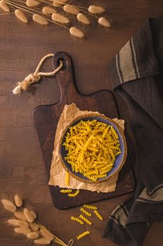 fusilli pasta in wooden cutting board on rustic kitchen countertop.