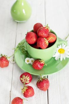 ripe strawberries from the garden in a green mug with white chamomile, fruity summer still life, close-up. High quality photo