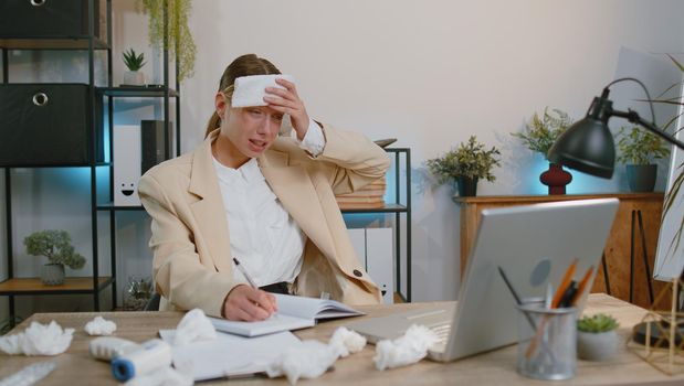 Sick ill businesswoman suffering from cold flu or allergy working on laptop at home office. Manager freelancer girl with towel on head blows sneezes wipes snot into napkin. Coronavirus quarantine