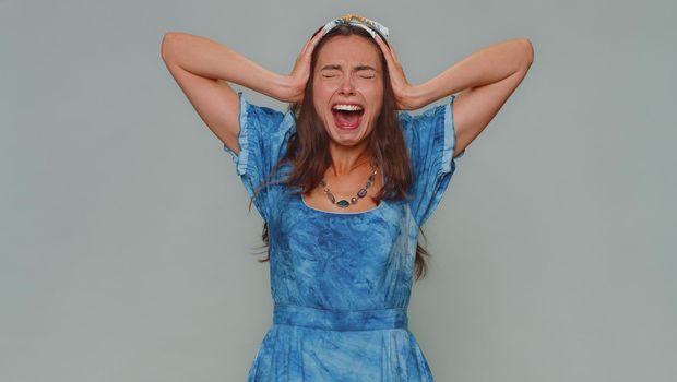 Angry sad young woman screams from stress tension problems feels horror hopelessness fear surprise shock expresses gestures rage. Adult stylish girl isolated alone on gray studio background indoors