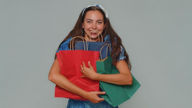 Happy young woman showing shopping bags, advertising discounts, smiling looking amazed with low prices, shopping on Black Friday holidays . Adult stylish girl isolated alone on gray studio background