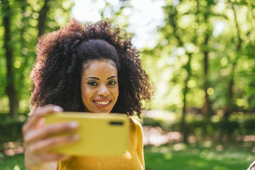 Pretty afro woman taking a selfie smiling in the forest. Selective focus.