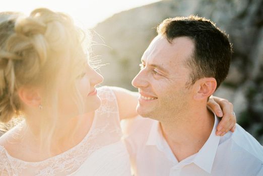 Bride hugs groom by the neck, sitting in his arms. Portrait. High quality photo