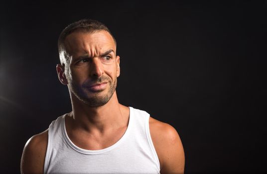 Distrustful athlete man in tank top. Close up. Black background.