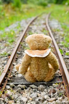 a cute brown teddy bear sits alone on empty mini-rails and looks into the distance, do-it-yourself toy. High quality photo
