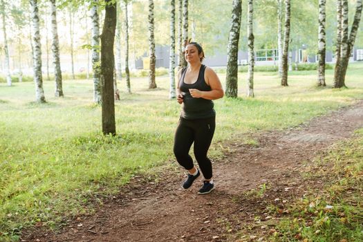 A charming brunette woman plus-size body positive practices sports in nature.