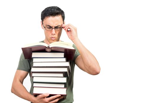 Clever male student adjusting glasses and reading book on stack during exam preparation against white background