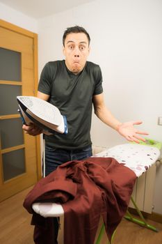 Man who does not know how to iron clothes, trying unsuccessfully to iron a shirt at home. Mid shot.