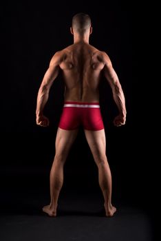 Vertical studio portrait of the back of a strong adult male in pants standing with black background