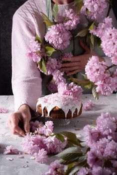 a woman decorates a homemade Easter cake with pink sakura flowers, spring blossom, a bouquet of pink sakura flowers on a table in a decorated spring room, a beautiful still life. High quality photo