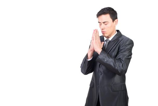 Thoughtful adult male with closed eyes wearing black formal suit praying with clasped hands against white background