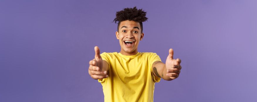 Close-up portrait of charismatic, happy friendly-looking hispanic man with dreads reaching hands forward to hold something, give hug or cuddle dearly, standing purple background.