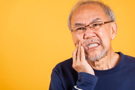 Dental pain. Portrait senior old man sad hand touching cheek suffering from toothache studio shot isolated on yellow background, Asian unhappy elder man problems with teeth pain, dental healthcare