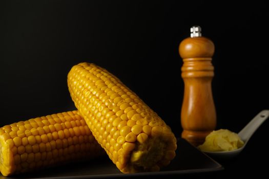 corn on the cob with pepper and butter in a white ceramic spoon isolated on black background