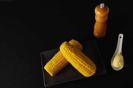 corn on the cob with pepper and butter in a white ceramic spoon isolated on black background
