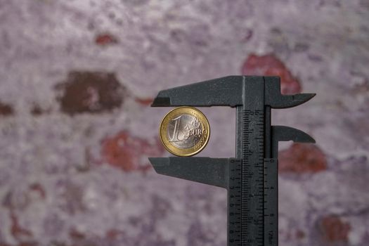 close-up of a euro coin held by a caliper at the bottom of a brick wall