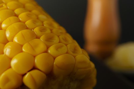 close-up macro shot of a fresh ear of corn with an out-of-focus pepper pot in the background