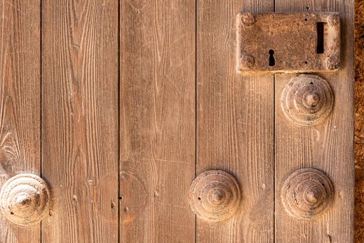 Closeup of wooden planks of door decorated with timber elements and rusted keyhole of doorway, in castle of Citadel of Almeria city in Spain in sunlight