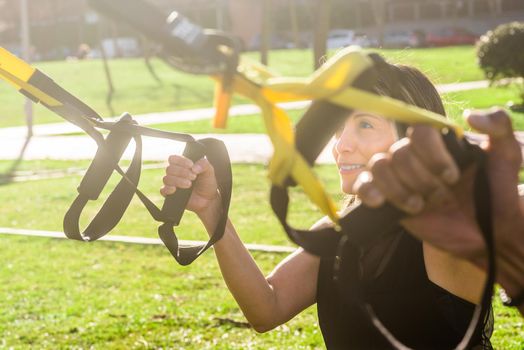 Fitness woman exercising with trx fitness straps in the park. Adult woman exercising outside.