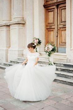Bride in a white dress stands in front of the church steps. High quality photo