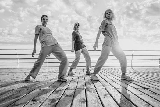 Dancing group of young talented freak women performing freestyle hip-hop moves. females enjoying modern dance expression. Outdoor training near sea or ocean during sunset. High quality photo