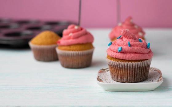 the muffin is on a saucer, decorated with cream and decor. kitchen utensils are in the background. The pink cream is applied in a spiral. Beautiful sweet dessert.