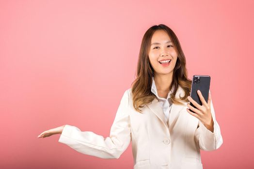 Happy Asian portrait beautiful cute young woman excited holding mobile phone blank screen presenting product with palm of hand at empty, studio shot isolated on pink background, female look camera