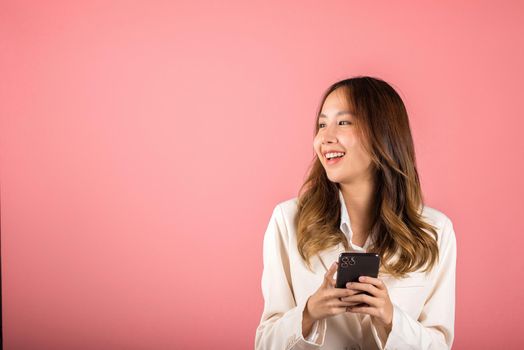 Female surprised and sms chatting internet online on smartphone studio shot isolated on pink background, Happy Asian portrait beautiful cute young woman teen smiling excited hold smart mobile phone