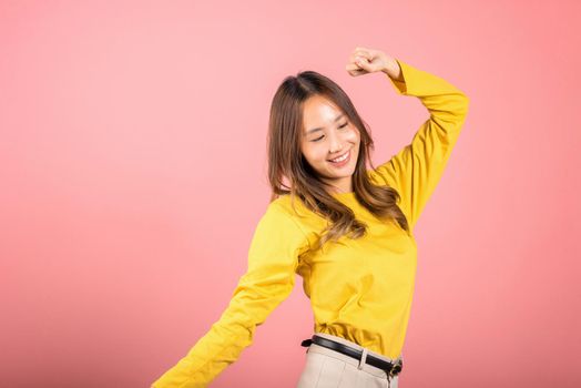 Asian young woman dancing with inspired face expression and raising hands up, Portrait of happy female model jocund in sneakers dancing, studio shot isolated on pink background, Time to relax