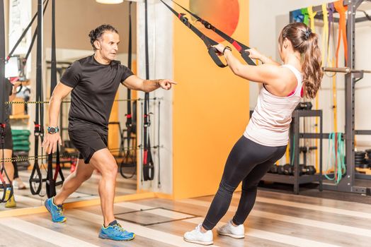 Athlete woman doing exercises with trainer with trx fitness straps in gym. Concept of trx training.