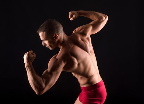 Muscular man on his back and shirtless, sticking out biceps. Mid shot. Black background.